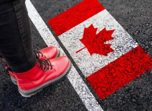 a woman with a boots standing on asphalt next to flag of Canada and border