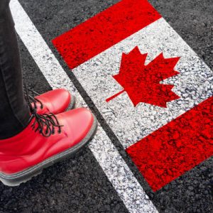 a woman with a boots standing on asphalt next to flag of Canada and border