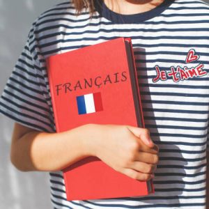 one white girl child schoolgirl with t-shirt with i love you in french and french textbook with french inscription and flag of France, foreign language learning concept.