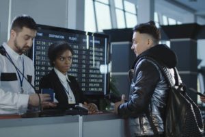 Men and women walking through counter with multiethnic employees in airport passing biometric and passport control.