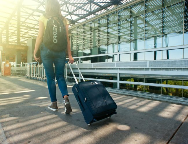 woman walking on pathway while strolling luggage
