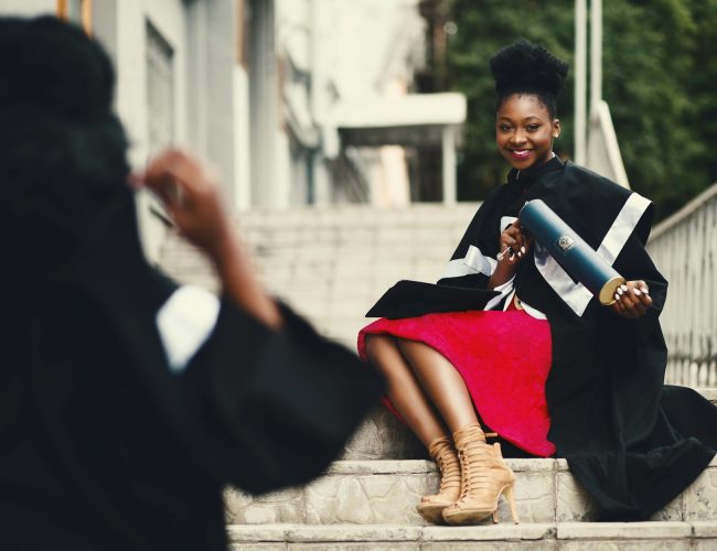woman wearing black graduation coat sits on stairs